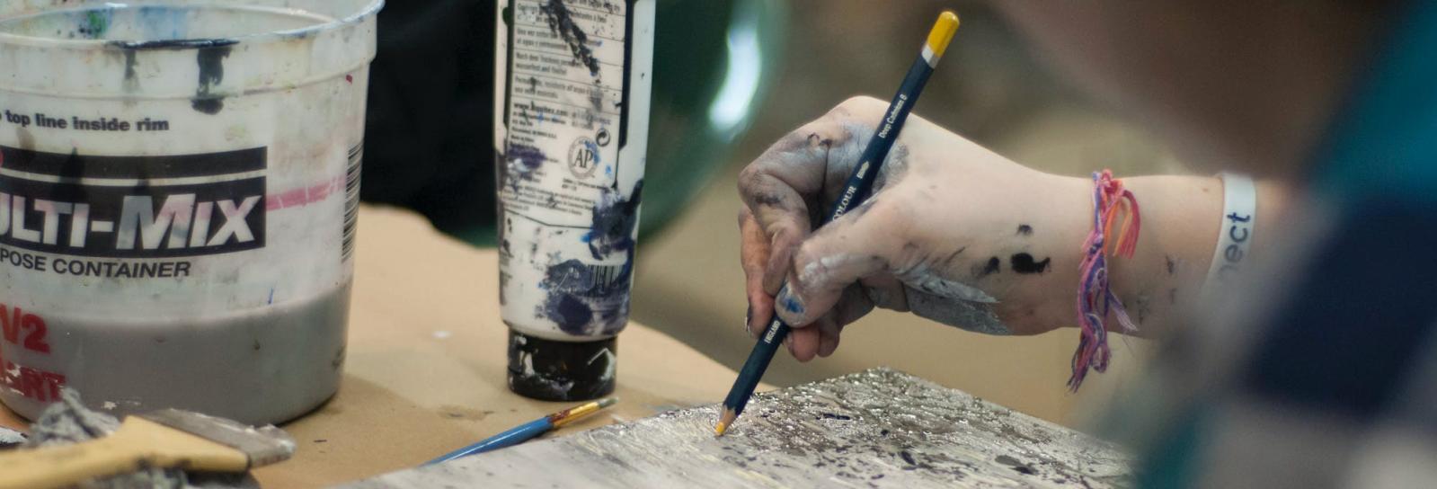 Et billede over skulderen på et ung menneske, som er i gang med at tegne eller male på et lærred.